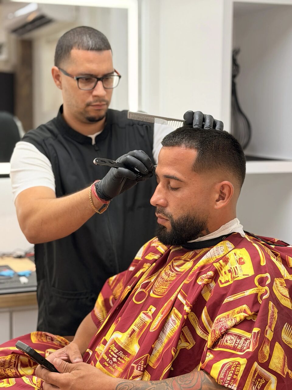 A barber in black gloves carefully detailing a client's haircut