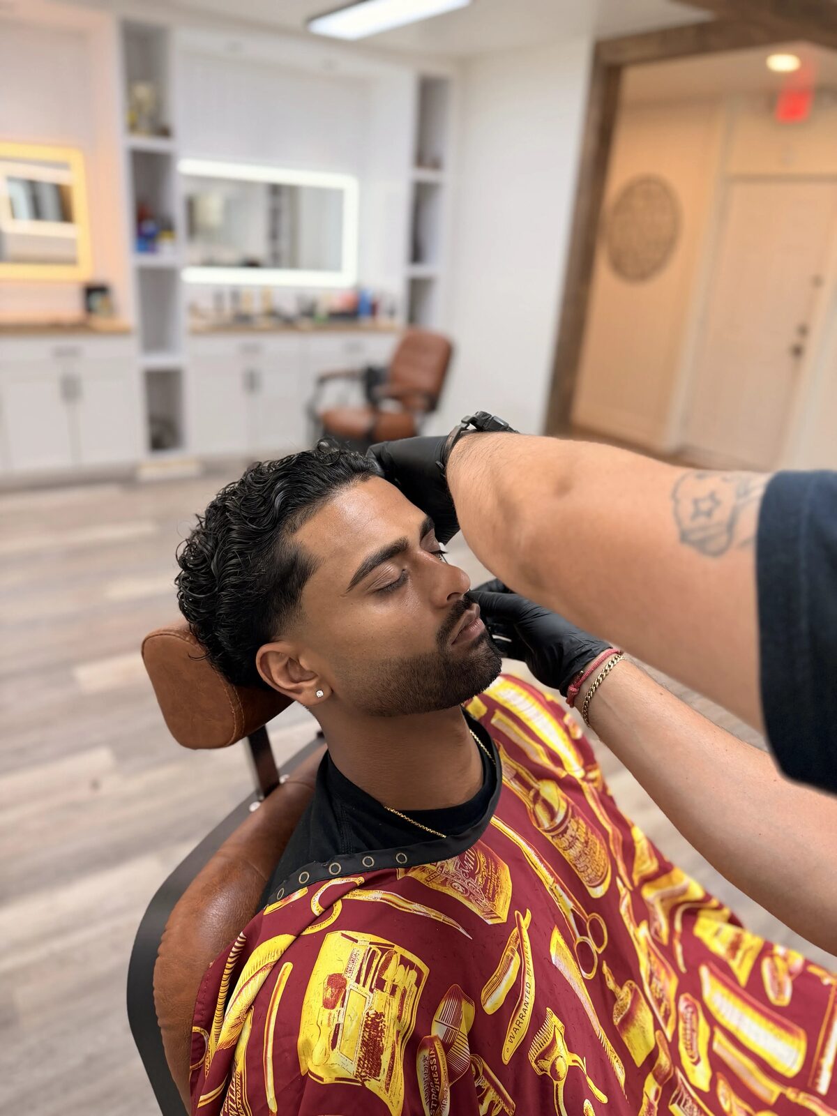 A barber shaping a client's beard line while the client reclines in a leather barber chair