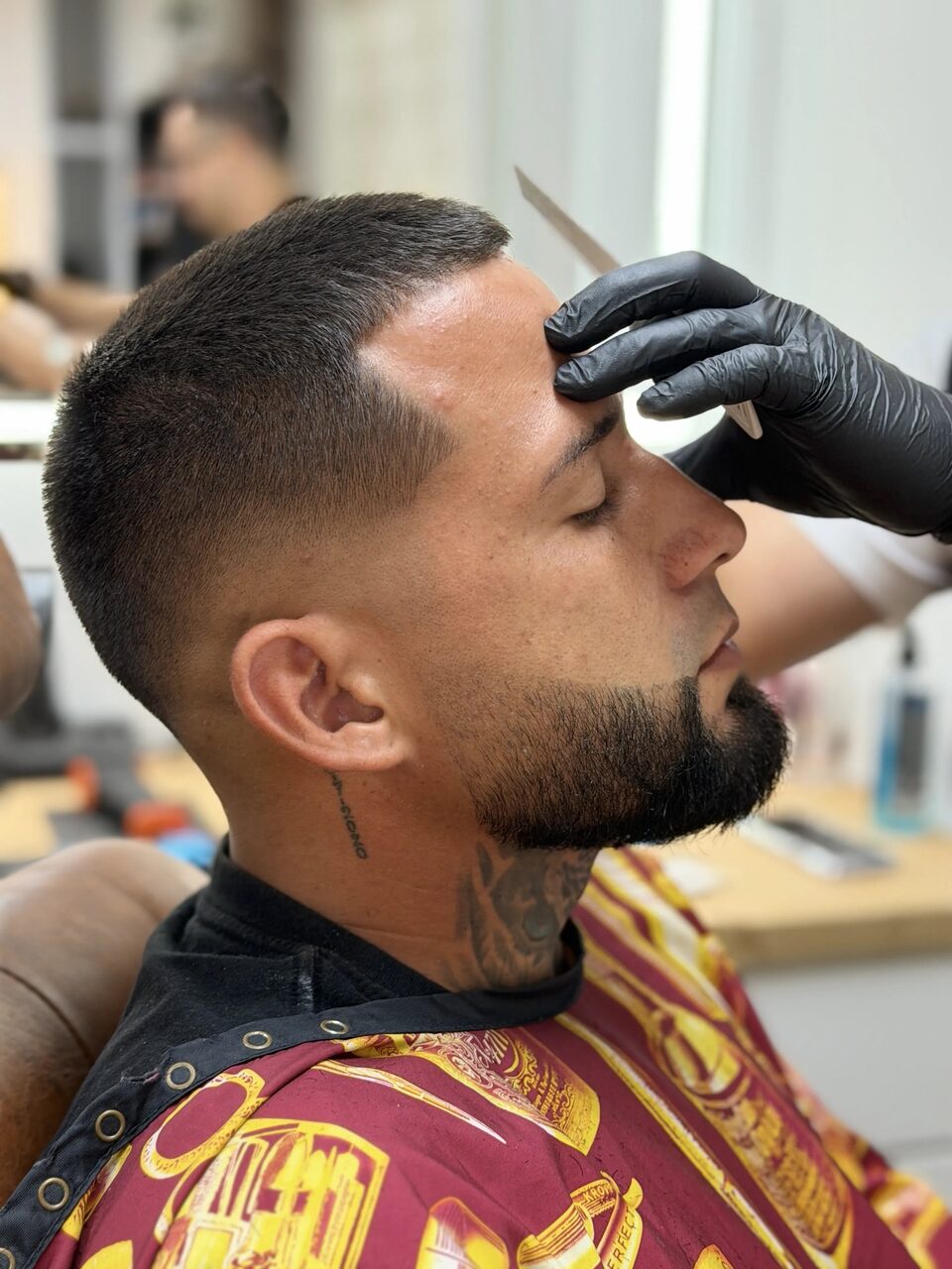 A gloved barber refining a client's hairline with a straight razor